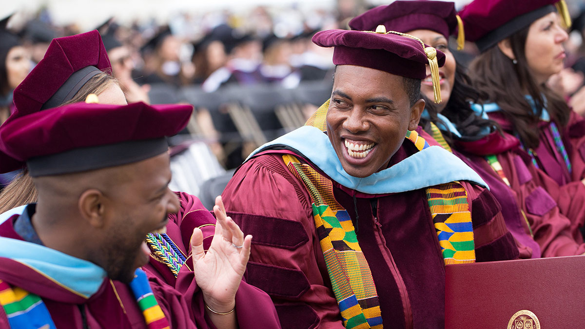 Graduate students smiling and talking at their seats before commencement begins