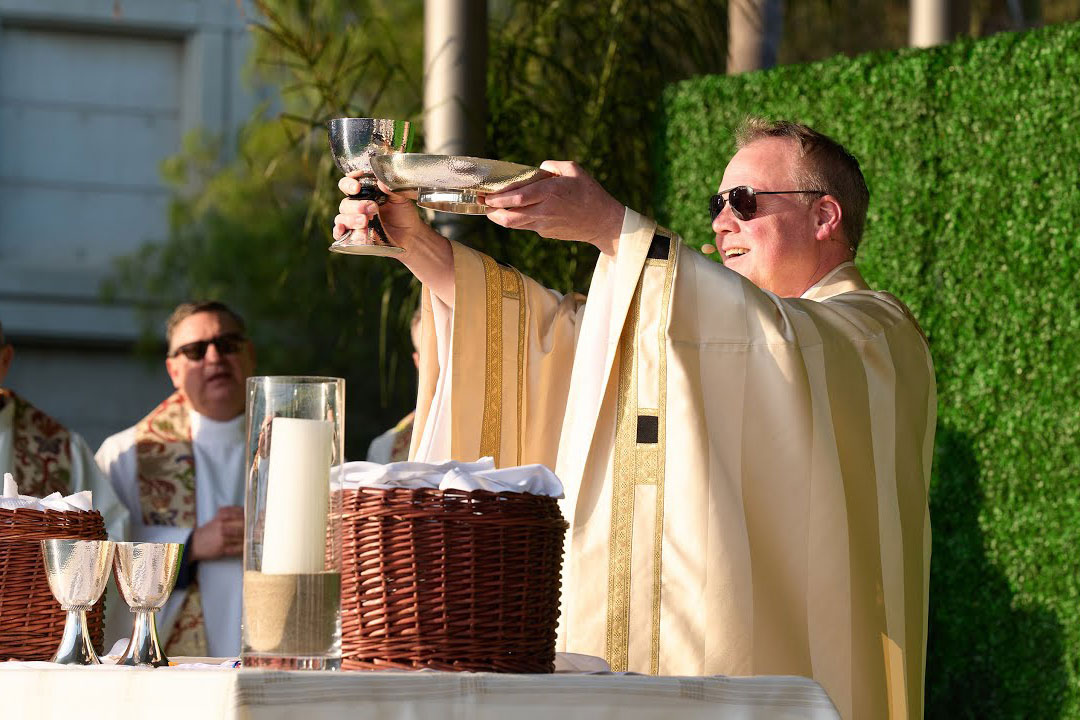 A priest on stage performing mass and smiling to the audience