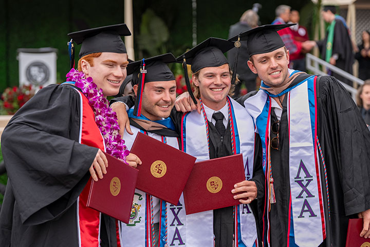 Four graduates holding up their diplomas and smiling