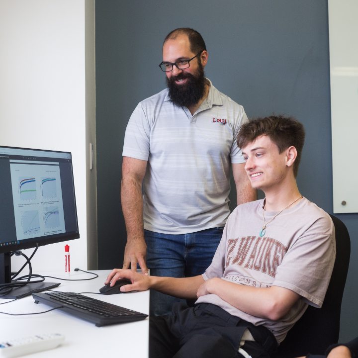 A faculty member and student stand beside a computer screen