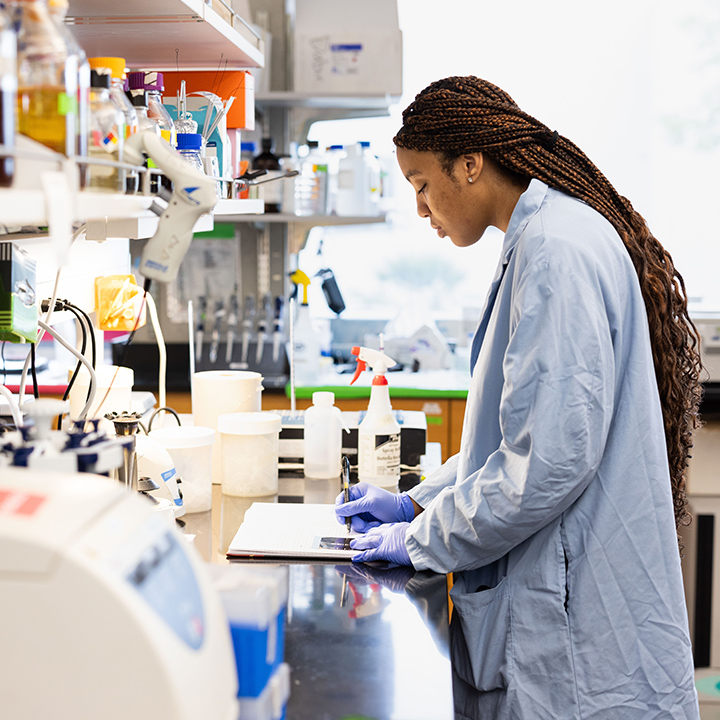An LMU Student Scientist writes notes in a lab