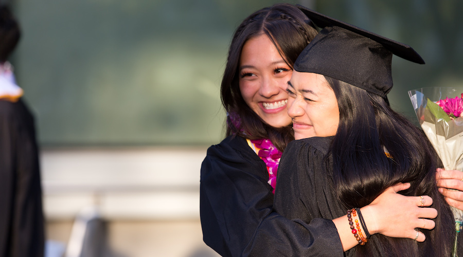 Two women in cap and gown embracing and posing for a photo